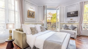 A bedroom with a bed, a sofa, a TV, and a balcony with a view of buildings.