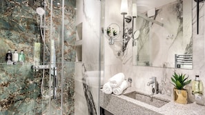 A modern bathroom with a glass-enclosed shower, marble walls, a sink with a mirror, and toiletries.