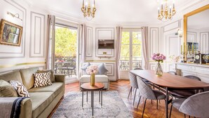 Une pièce comprenant un canapé, une table à manger avec des chaises, un lustre, un téléviseur et donnant sur l’extérieur.