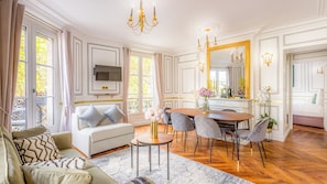 A spacious living room with a sofa, dining table, chairs, and a TV. - Merveil - Luxury Suite - Louvre -Sebastopol I (Paris)