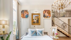 Une chambre spacieuse avec un grand lit, un lustre, un escalier et des tableaux de style classique.