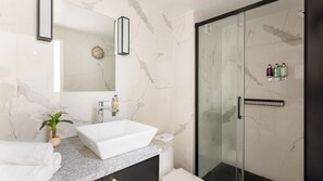 A modern bathroom with a white sink, marble tiles, a glass shower enclosure, and a small potted plant. - Merveil - Luxury Suite - Louvre - Aboukir II (Paris)