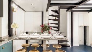 A modern kitchen with a central island, granite countertops, gold bar stools, and a decorative flower arrangement. - Merveil - Luxury Suite - Louvre - Aboukir II (Paris)