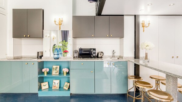 A modern kitchen with teal cabinetry, a coffee machine, and bar stools. - Merveil - Luxury Suite - Louvre - Aboukir II (Paris)