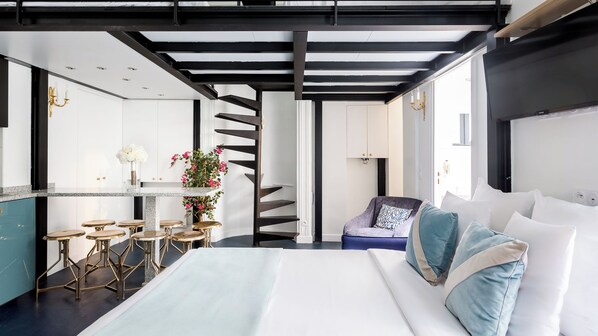Una habitación de hotel moderna con cama, zona de estar con taburetes, una escalera y un ventanal grande.