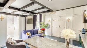 A modern living room with a blue sofa, a grey armchair, and a marble coffee table. There is a vase with red flowers and a mirror on the wall. - Merveil - Luxury Suite - Louvre - Aboukir II (Paris)