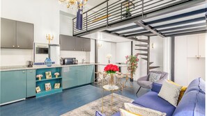 A modern kitchen with teal cabinets, a dining area with a round table, and a staircase leading to an upper level. - Merveil - Luxury Suite - Louvre - Aboukir II (Paris)