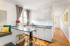 A modern kitchen with white cabinets, a marble countertop, and a built-in island with stools.