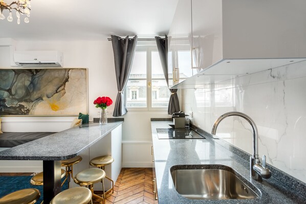 A modern kitchen with a marble countertop, stainless steel sink, and a herringbone wood floor.