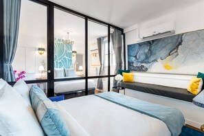 Habitació d'hotel amb un llit gran, una vista a través d'una porta de vidre i una obra d'art modern a la paret.