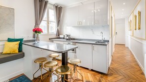 Une cuisine moderne avec des meubles blancs, un plan de travail en marbre et un îlot central intégré avec des tabourets.