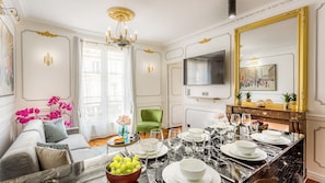 A dining area with a marble table set for a meal, a green armchair, and a chandelier. - Merveil - Luxury Suite - Louvre - Sebastopol II (Paris)