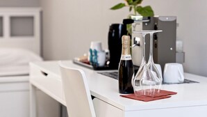 A neatly arranged hotel room with a white desk, a bottle of champagne, a glass, and a vase with a yellow flower. - Bed and Best Triple/Quadruple deluxe (Roma)