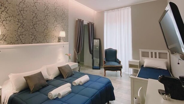 A hotel room with a bed, a desk, a chair, a TV, and a mirror. - Bed and Best Triple/Quadruple deluxe (Roma)