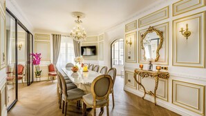 A formal dining room with a long table, chairs, a chandelier, and a large mirror. - Merveil Signature Suite - Valois - Louvre view (Paris)