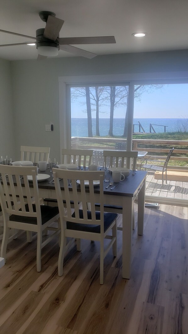 A dining area with a view of the sea, white chairs, a table set for four, and a ceiling fan.