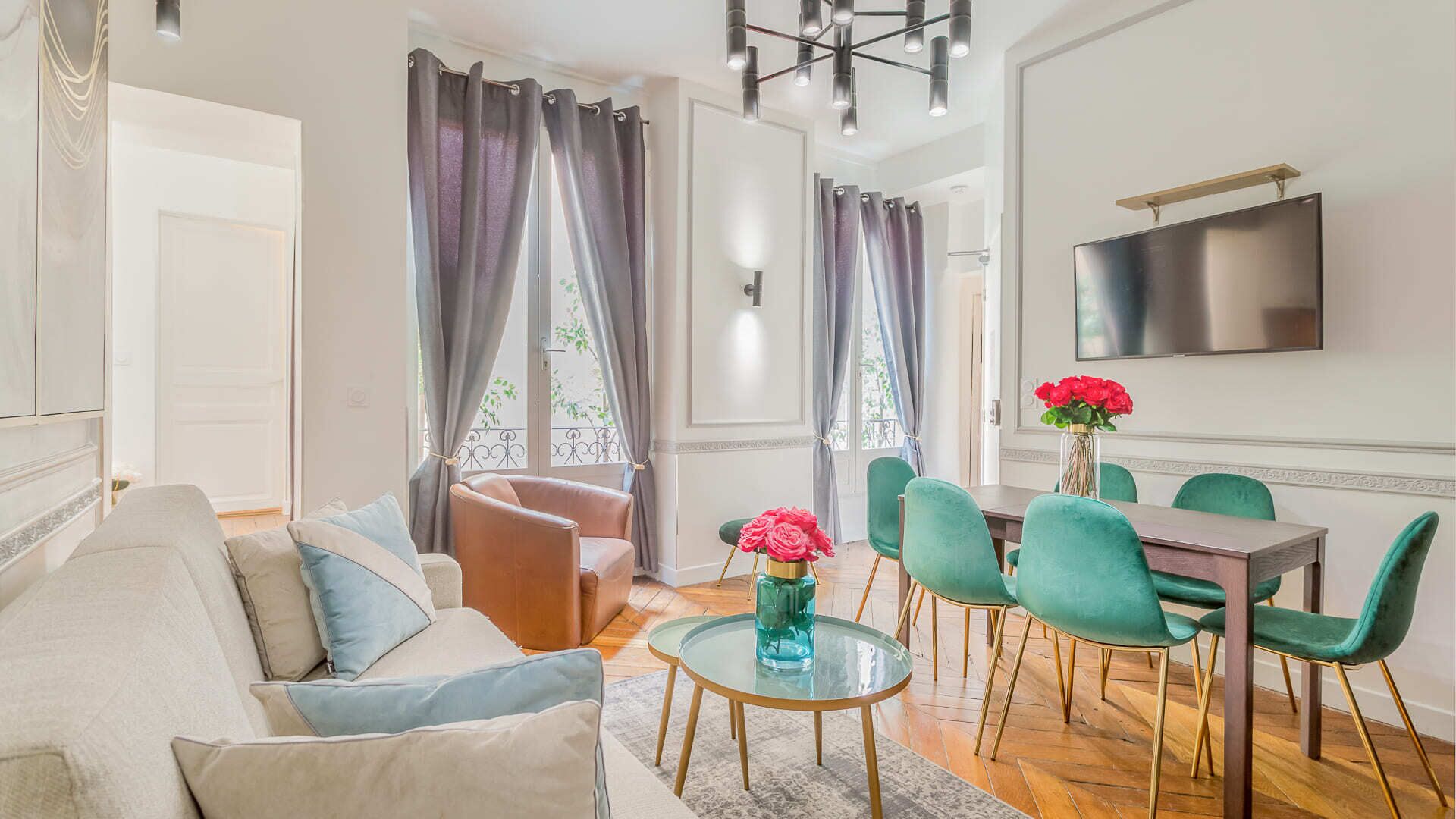 A modern living room with a sofa, a glass coffee table, and a dining area with green chairs and a wooden table.