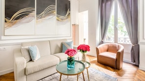 Relax in this inviting living room with a sofa, armchair, and coffee table, surrounded by a beautiful abstract painting and a vase with fresh flowers.