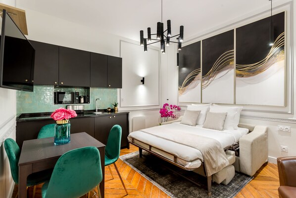 A modern bedroom with a bed, a desk, and a kitchenette.