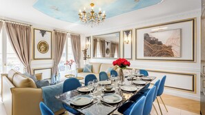 Comedor con una mesa de mármol dispuesta para seis comensales, sillas tapizadas en azul y una araña.