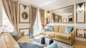 Un salón lujoso con un sofá beige, una mesa de centro con pasteles y un espejo grande.