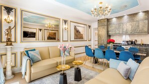 Un salón lujoso con un sofá color crema, sillas azules, una mesa de comedor y una zona de cocina con encimeras de mármol.