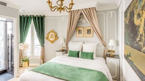 Un dormitorio lujoso con una cama grande, cortinas verdes y beige, una araña y cuadros en la pared.