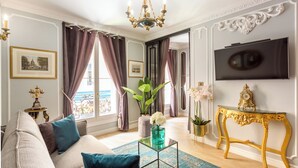 Una sala de estar con un sofá, una mesa de centro con un florero, un televisor y una consola dorada.