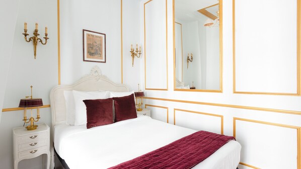 A neatly arranged bedroom with a white bed, a red throw blanket, a nightstand with a lamp, and a framed picture on the wall.