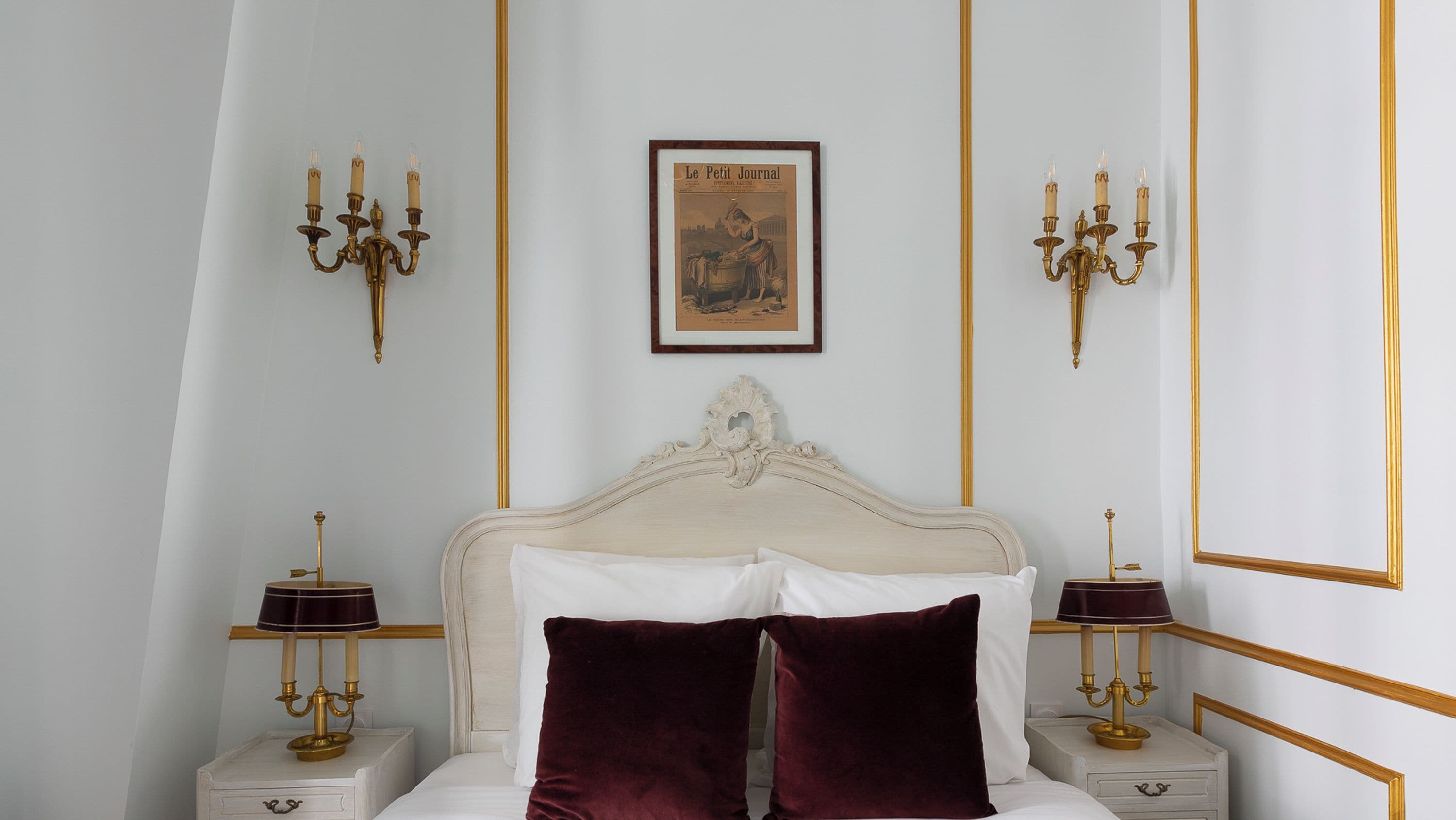 A bedroom with a large bed, ornate wall sconces, a framed picture, and a mirror.