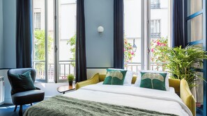 Une chambre d’hôtel avec un lit, une chaise, une petite table et une plante en pot.