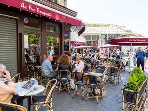 Un café en plein air avec des chaises et des tables en osier, une marquise rouge sur laquelle on peut lire « Au Père Tranquille », et une enseigne indiquant « Rue Rambuteau ».