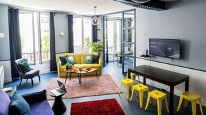 Een moderne woonkamer met een bank, een salontafel, een televisie en een eethoek met krukken.