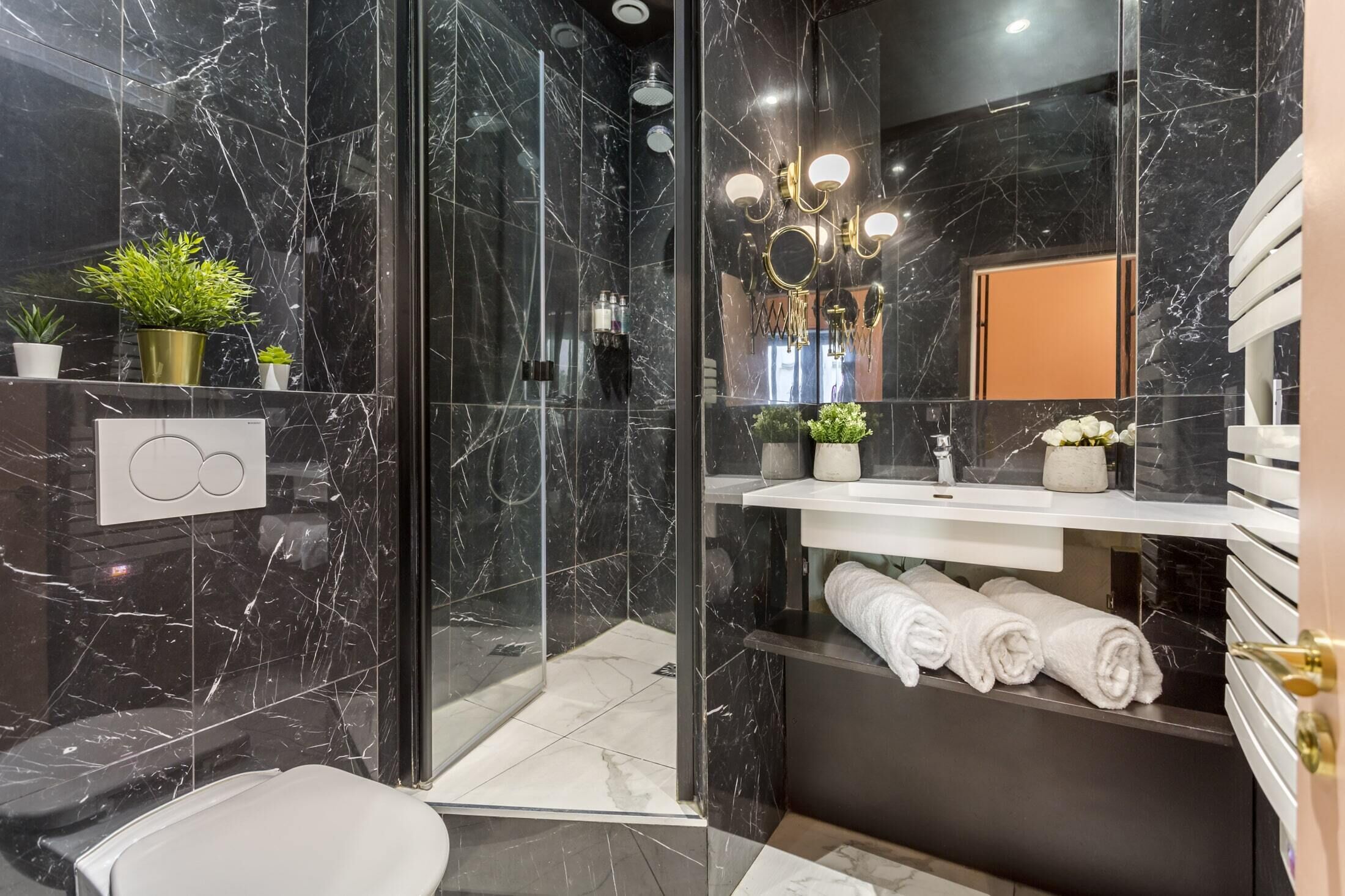 Une salle de bain moderne avec une douche à parois de verre, des murs en marbre, un lavabo blanc et un miroir.