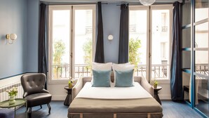 Un dormitorio con una cama, una silla, una mesita y un ventanal con cortinas.