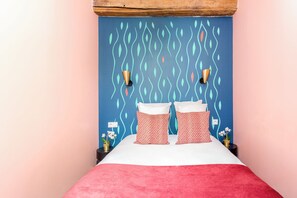 Een bed met een rode deken, twee kussens met een patroon en een blauwe muur met bladmotieven.