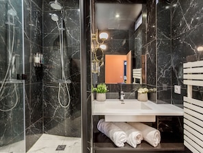 Une salle de bain moderne avec une douche à parois de verre, un meuble-lavabo blanc avec un miroir et deux serviettes posées sur le sol.