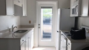 A modern kitchen with white cabinets, a stainless steel sink, a microwave, and a stove. There is a door leading to an outdoor area. - Steps to Siesta Key BEACH!  Pool, Tennis Court, Shuffle Board, Pickle Ball! (Siesta Key)