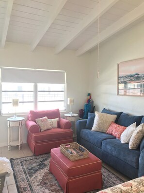 A living room with a red sofa, a blue sofa, and a patterned rug. There are two side tables with lamps, and a framed picture on the wall.