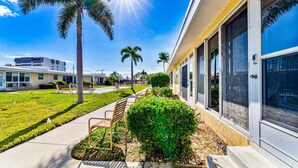 A modern building with a covered outdoor seating area, palm trees, and a clear blue sky. - Steps to Siesta Key BEACH!  Pool, Tennis Court, Shuffle Board, Pickle Ball! (Siesta Key)