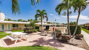A patio area with a white picnic table, a barbecue grill, and palm trees. - Steps to Siesta Key BEACH!  Pool, Tennis Court, Shuffle Board, Pickle Ball! (Siesta Key)
