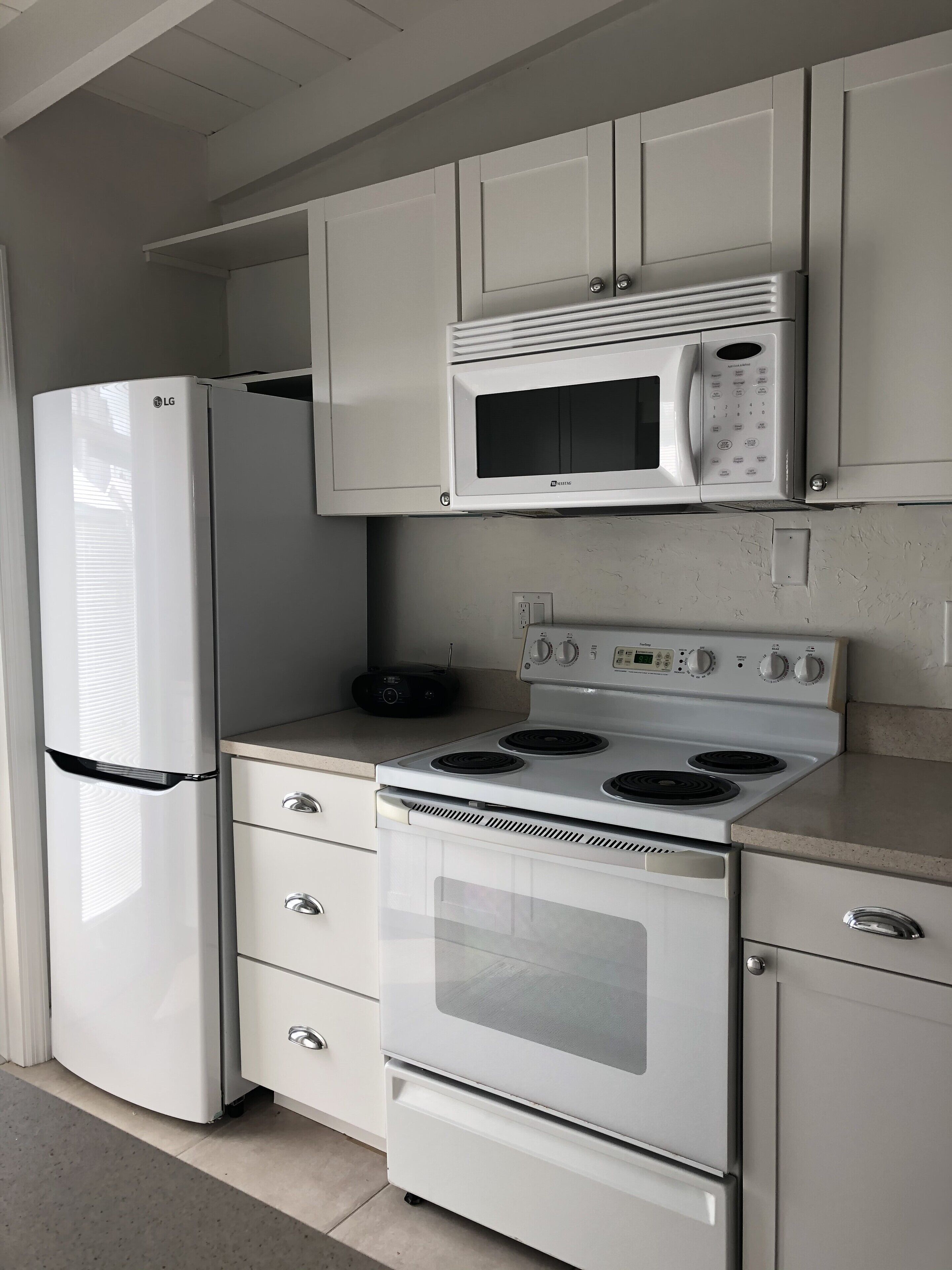 A kitchen with white cabinetry, a built-in microwave, a stove, and a refrigerator.