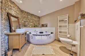 Une salle de bain moderne avec un mur en pierre, un meuble-lavabo en bois, une baignoire sur pieds et des toilettes blanches.