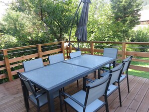 Une terrasse avec une table rectangulaire et six chaises, entourée d’une clôture en bois et d’une végétation luxuriante.