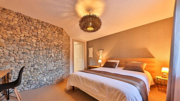 Une chambre d’hôtel avec un mur en pierre, un lit recouvert d’une courtepointe à rayures, une chaise, une petite table et une lampe fixée au mur.