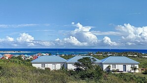 A coastal view with three white buildings with blue roofs, surrounded by greenery and a clear blue sky. - Paradise View, Maison créole avec piscine privée à 5 min d`Orient Bay (Orient Bay)