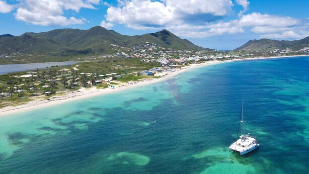 A coastal town with a clear blue sea, a sandy beach, and a sailboat anchored near the shore. - Paradise View, Maison créole avec piscine privée à 5 min d`Orient Bay (Orient Bay)