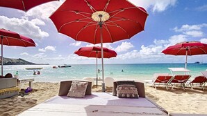 A beachside lounge area with red umbrellas, lounge chairs, and a view of the ocean.