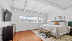 A bedroom with a bed, a bench, a dresser, a TV, and a window with blinds. - Dickson St. Hideaway (Fayetteville)