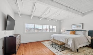 A bedroom with a bed, a bench, a dresser, a TV, and a window with blinds. - Dickson St. Hideaway (Fayetteville)